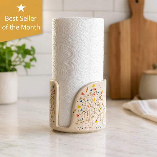 A ceramic paper towel holder with a colorful tree design, holding a white paper towel roll, set on a marble countertop with a blurred kitchen background.