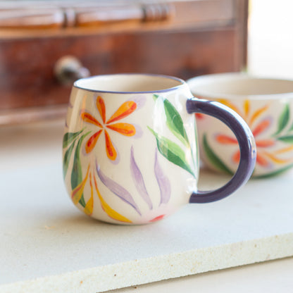 Elegant Blossom Mug featuring vibrant hand-painted flowers, displayed with a wooden chest in the background enhancing its handmade charm