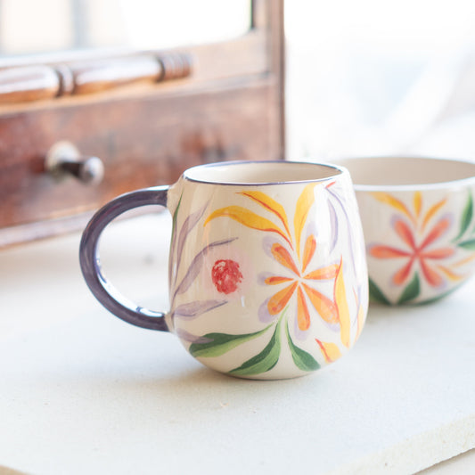 Handcrafted Blossom Mug with orange and purple floral design, set on a counter showcasing its unique hand-painted artistry.