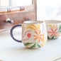 Handcrafted Blossom Mug with orange and purple floral design, set on a counter showcasing its unique hand-painted artistry.